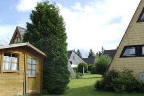 A wooden cabin with a sloped roof, surrounded by a well-maintained lawn and a tall evergreen tree. - Holiday home with 2 bedrooms (Lichtenberg)