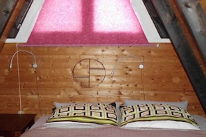 Une pièce avec un plafond en bois, un lit recouvert d’une literie à motifs et un motif circulaire sur le mur.