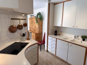 A modern kitchen with white cabinets, a black stove, and a red chair. - Apartment DA 27 by Interhome (Ascona)