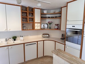 Una cucina compatta con mobili bianchi, forno integrato e piano di lavoro in legno.