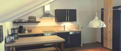 A compact kitchen with a wooden table, a built-in oven, and a hanging light fixture.