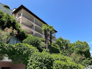 A multi-story building with balconies, surrounded by lush greenery and palm trees. - Lago Maggiore by Interhome (Brissago)