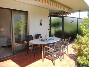 An outdoor patio with a round table, chairs, and a glass door leading to a balcony. - Aphrodite by Interhome (Brissago)