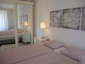 A bedroom with a bed, a bedside table, a lamp, and wall art. - Aphrodite by Interhome (Brissago)