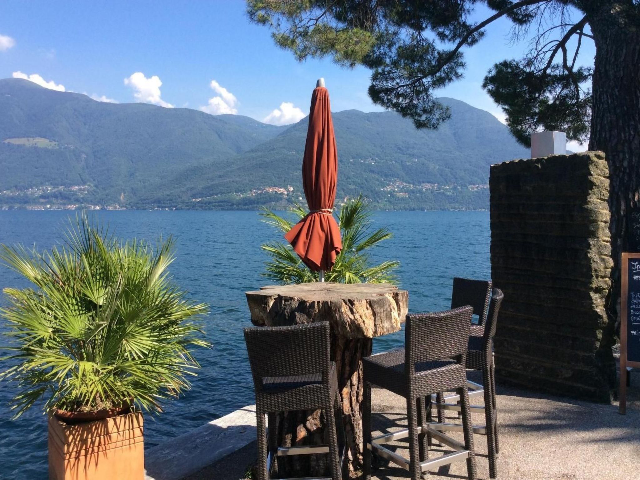 Een terras met een tafel en stoelen, met uitzicht op een waterpartij en bergen.
