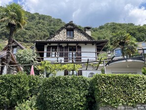 A traditional stone house with a balcony, surrounded by lush greenery and hills. - Rustico Al Torchio by Interhome (Locarno)