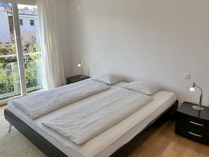 A modern bedroom with a large bed, two bedside tables, and a view of a balcony. - Bicledro by Interhome (Ascona)