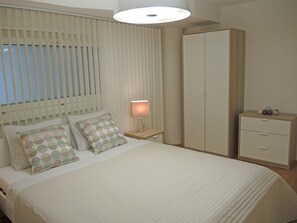 Een slaapkamer met een bed, nachtkastjes, een garderobe en een lamp.