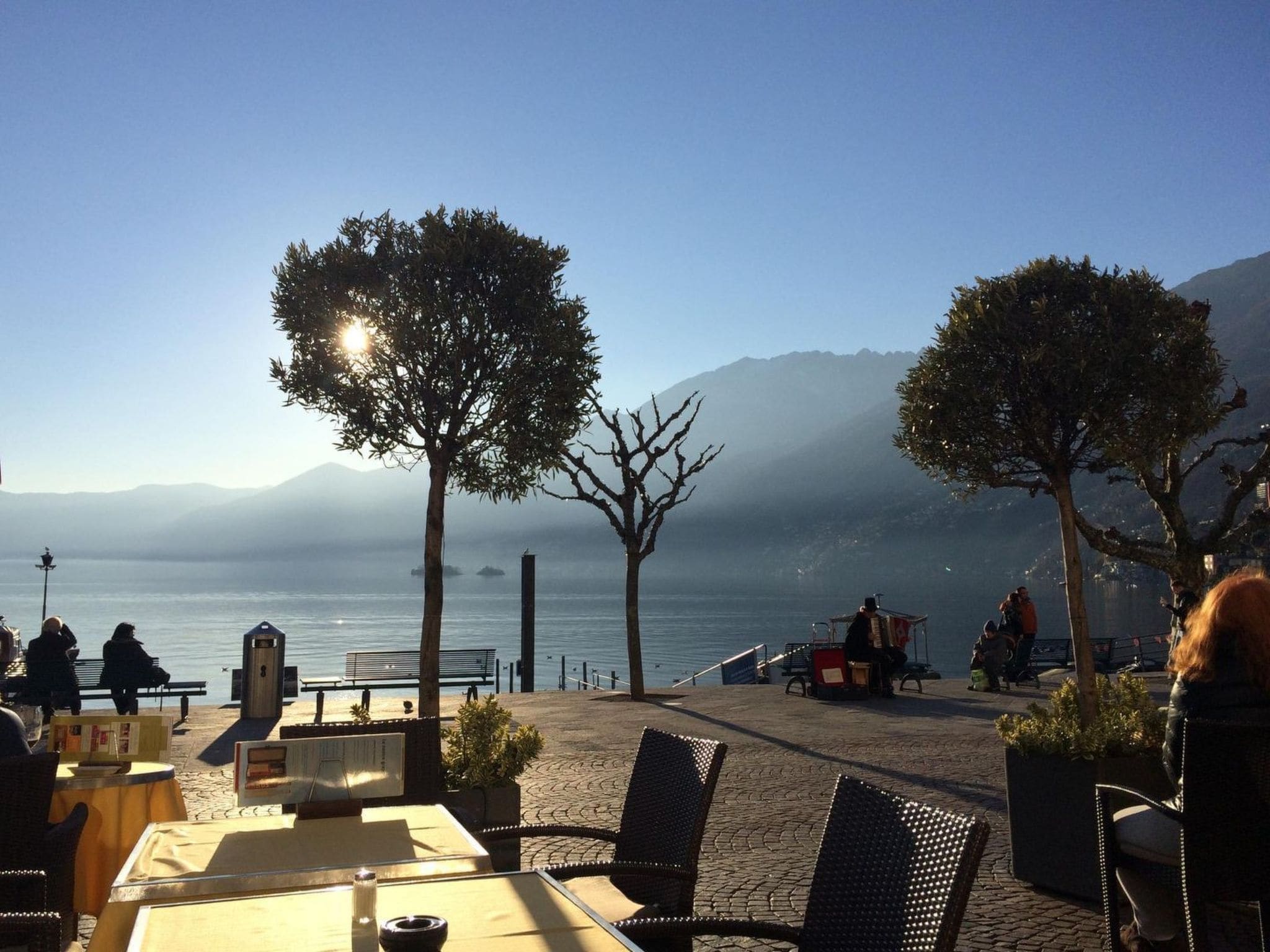 An outdoor seating area with tables and chairs, overlooking a body of water and mountains.