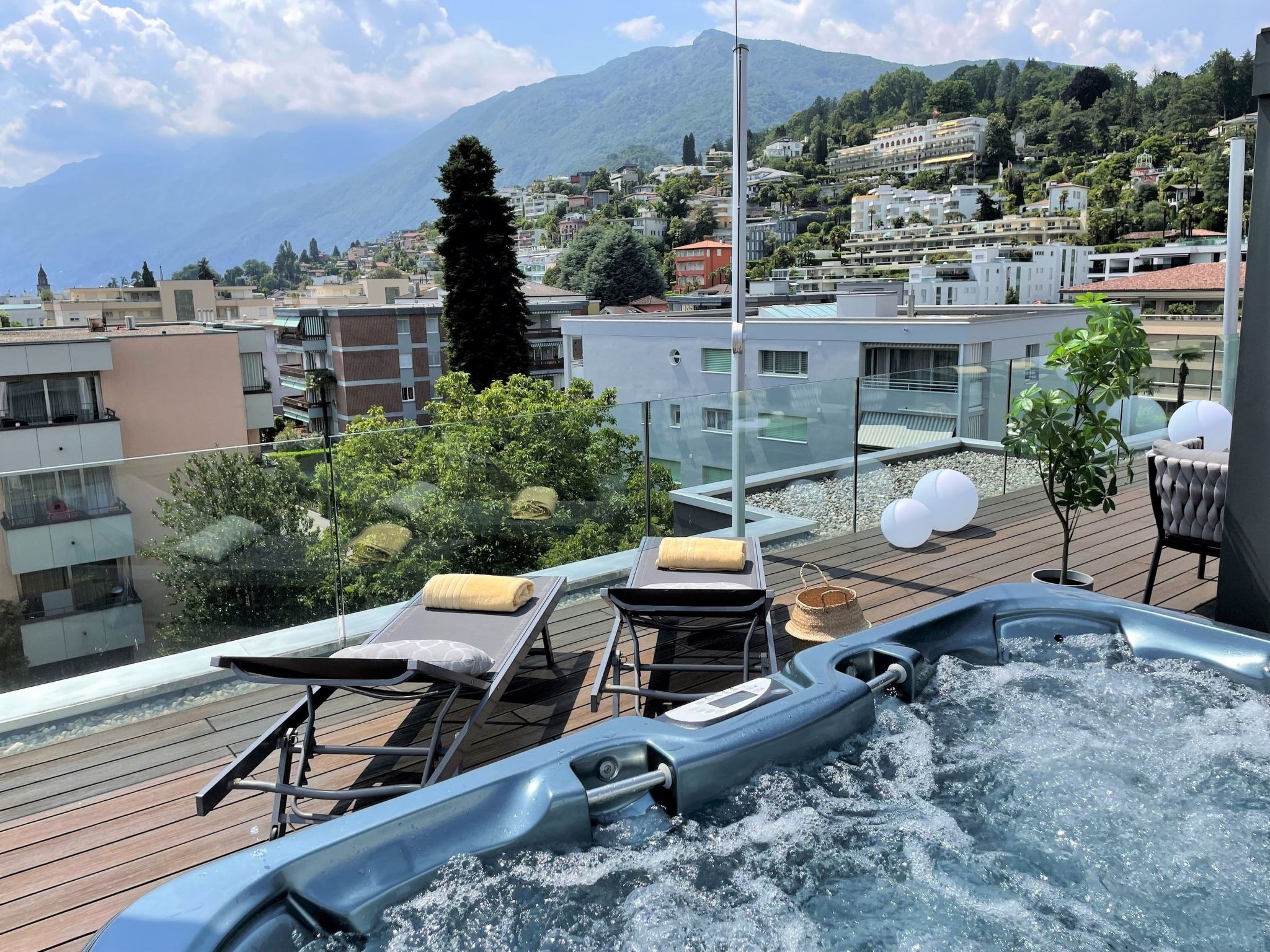 A rooftop terrace with a hot tub, lounge chairs, and a view of the cityscape and mountains.