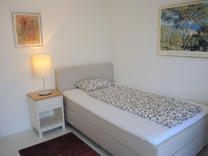 Ein Einzelbett mit einem gemusterten Überwurf, ein Nachttisch mit einer Lampe und ein gerahmtes Bild an der Wand.