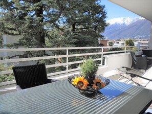 Ein Balkon mit Tisch, Stühlen und einem Topf mit Sonnenblumen.
