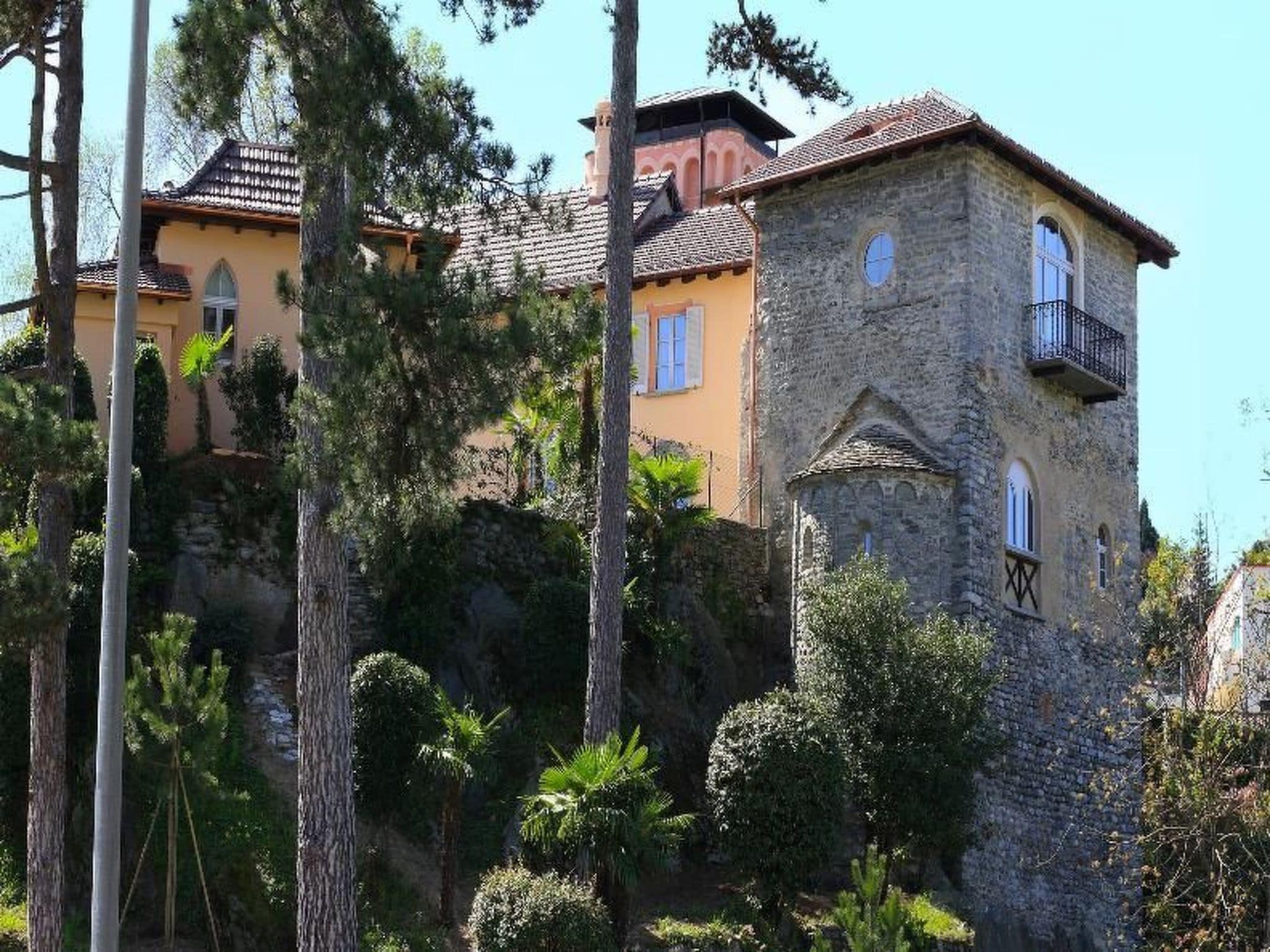 A multi-story building with a stone facade and a yellow upper section, surrounded by trees.