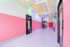 A hallway with a modern design, featuring a combination of white and pink walls, a marble floor, and a ceiling with recessed lighting.