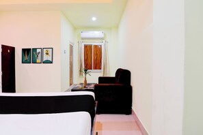 A hotel room with a bed, a chair, a small table with a vase, and a window with curtains. - Hotel O Murshidabad Junction Berhampore (Lalbag)