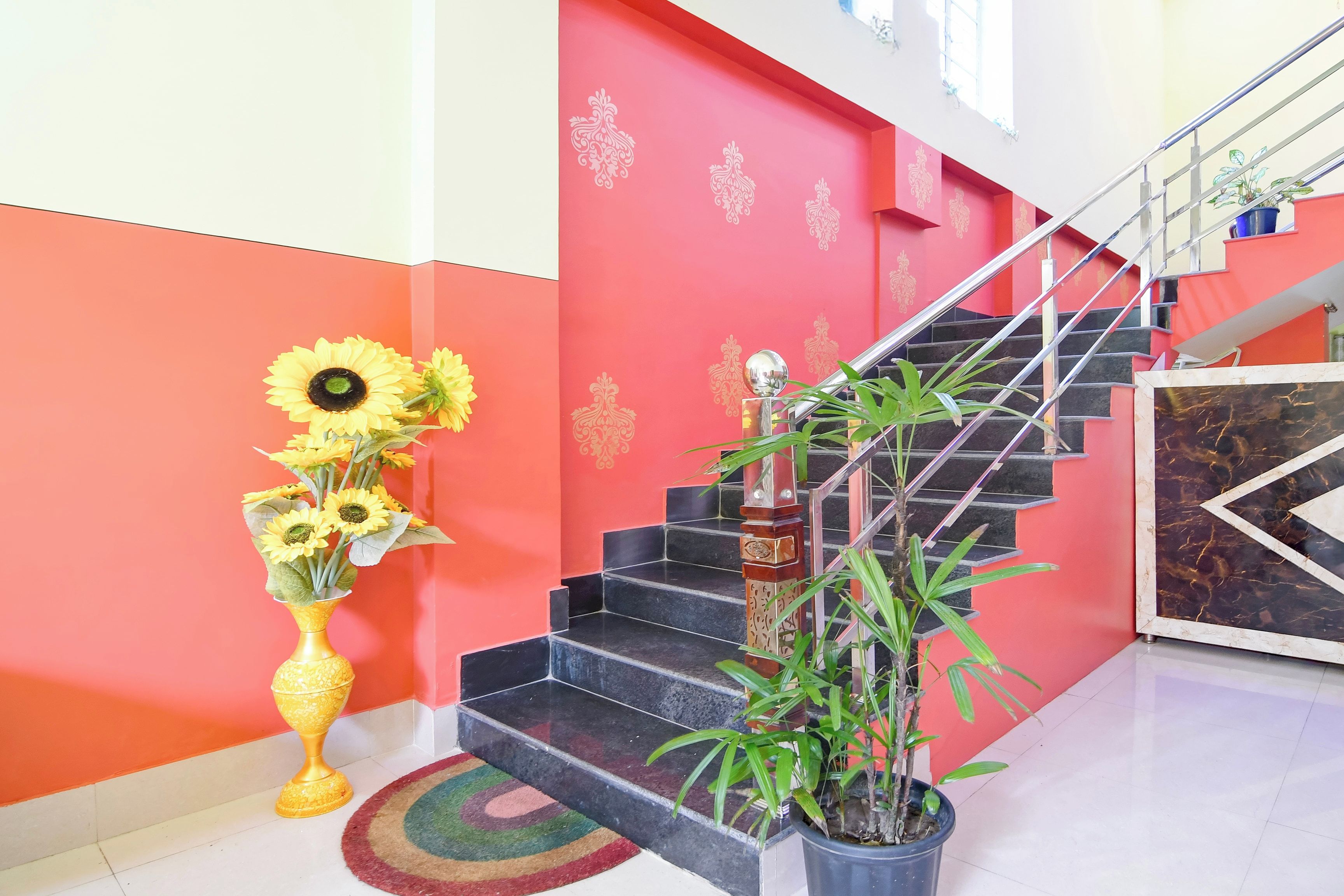 A staircase with a red wall and a decorative golden emblem, a vase with sunflowers, and a potted plant.