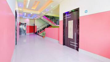 A brightly lit hallway with a staircase, a door with a room number sign, and a wall-mounted fire extinguisher.