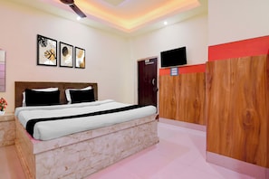 A bedroom with a bed, a wooden wardrobe, a television, and wall art.