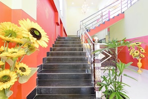 A staircase with black steps, a handrail, and a railing. Sunflowers are placed on the left side of the stairs.
