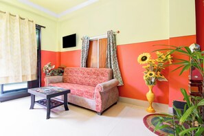 Una sala de estar con sofá, mesa de centro, televisor y un florero con girasoles.