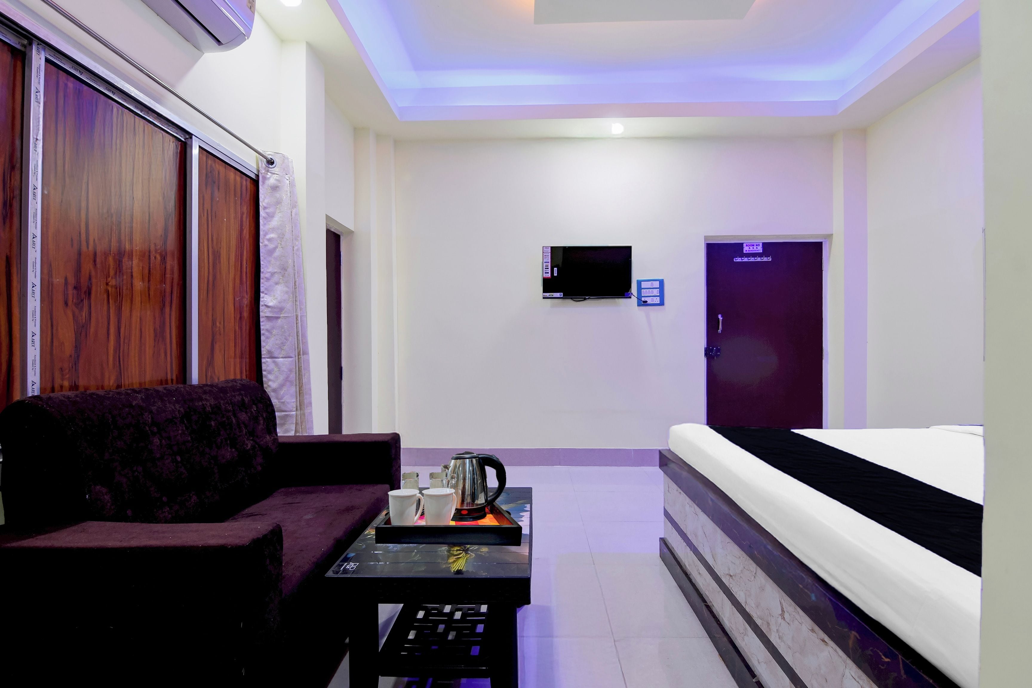 A hotel room with a sofa, a coffee table with a kettle, a TV, and a bed.