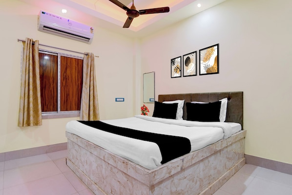A bedroom with a bed, a ceiling fan, an air conditioner, a window with curtains, and wall-mounted artwork.