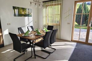 Een eetgedeelte met een tafel voor vier personen, stoelen, een schilderij aan de muur en uitzicht door het raam.