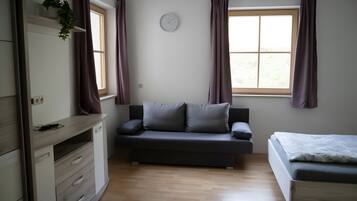 Et moderne, minimalistisk værelse med en sofa, en seng, et skrivebord og et vindue med gardiner.