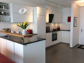 A modern kitchen with white cabinetry, a wooden countertop, a red kettle, and a vase with yellow flowers. - Apartment Nibbio by Interhome (Minusio)