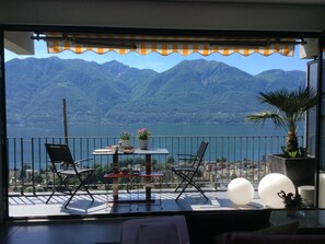 A balcony with a table, chairs, and potted plants, overlooking a lake and mountains. - Apartment Nibbio by Interhome (Minusio)