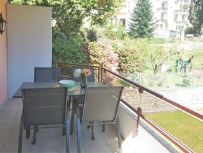 A balcony with a table and chairs, a vase with flowers, and a view of a garden and buildings. - Apartment Onyx by Interhome (Locarno)
