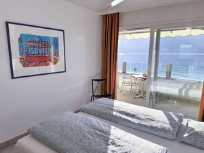A hotel room with a bed, a framed artwork, a chair, and a balcony with a view of the sea. - Residenza Acapulco I by Interhome (Porto Ronco)