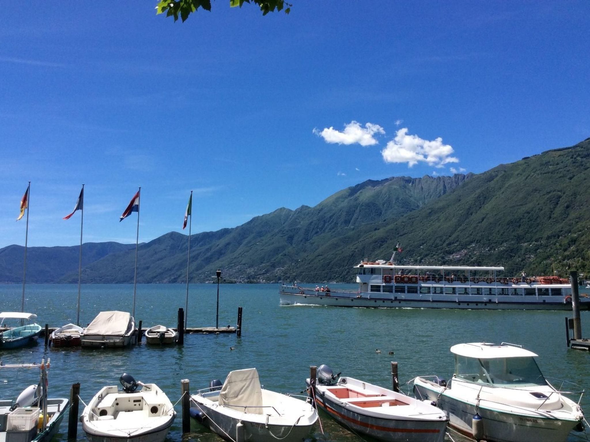A marina with boats docked, a large ferry, and mountains in the background.