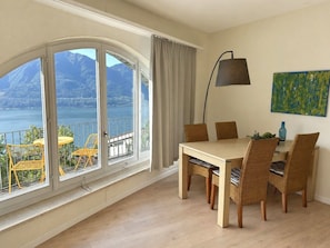 Ein Essbereich mit Blick auf einen See und Berge, ein Tisch mit Stühlen, eine Lampe und ein Bild an der Wand.