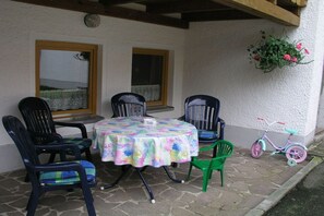 Un patio con una mesa redonda, cuatro sillas, una bicicleta y una maceta colgante con flores.