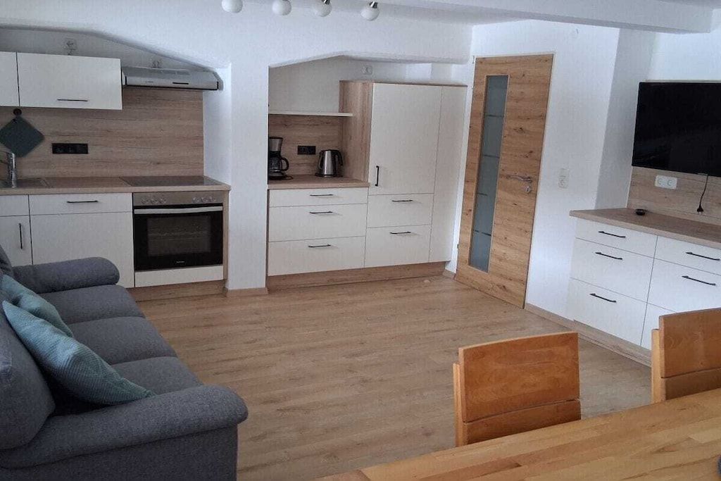 A modern kitchen with white cabinetry, a built-in oven, and a flat-screen TV.