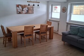 Un comedor con una mesa y sillas de madera, un sofá gris y un reloj fijado a la pared.