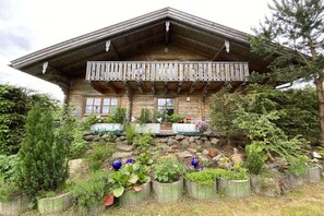 A wooden cabin with a balcony, surrounded by a garden with various plants and flowers. - Holiday home with 5 bedrooms (Riedlhütte)