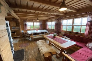 A wooden cabin interior with a dining table, benches, a sofa, and large windows. - Holiday home with 5 bedrooms (Riedlhütte)