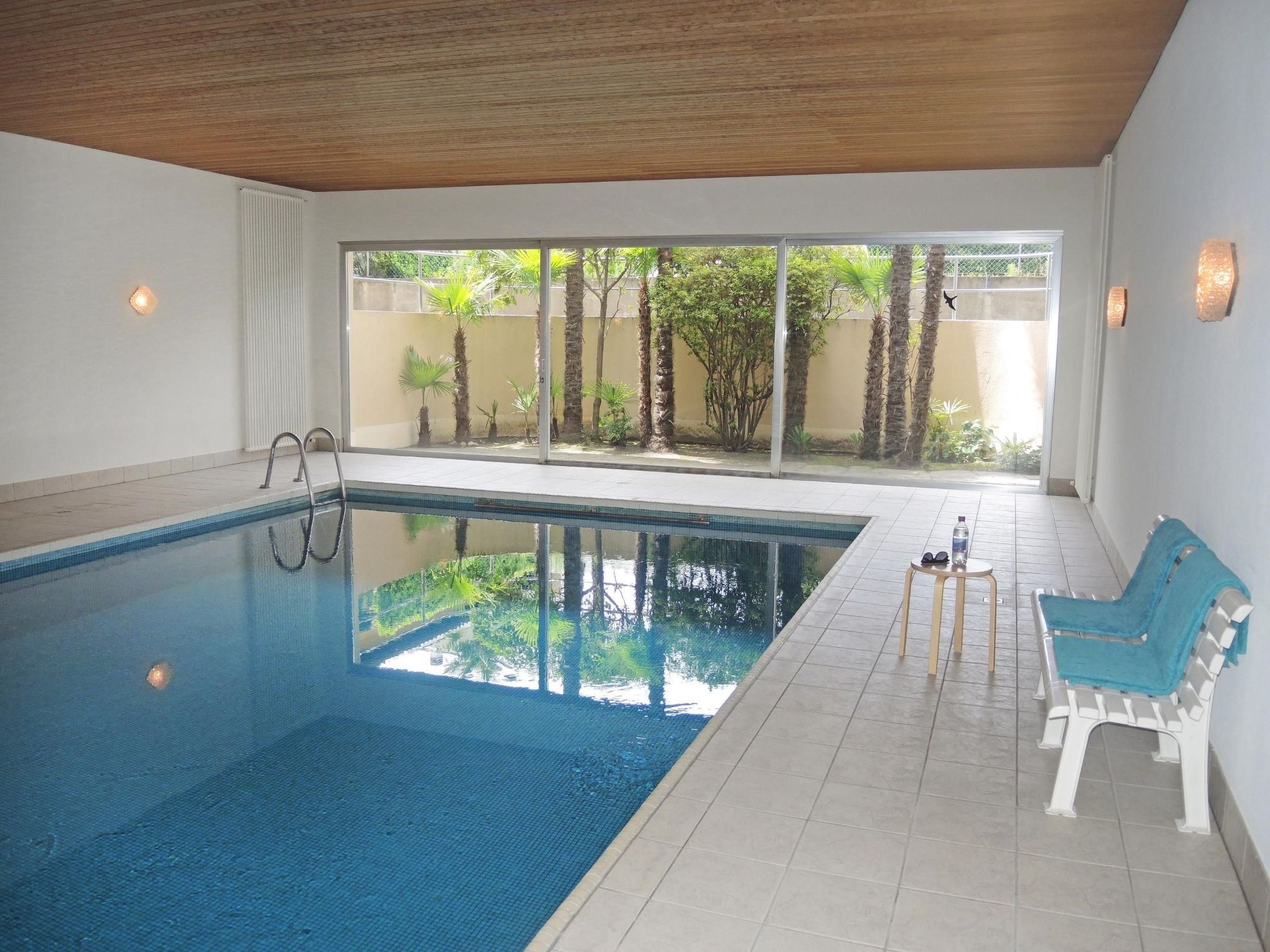 A swimming pool with a clear view of the outdoors, a bench, and a pair of sunglasses on the bench.