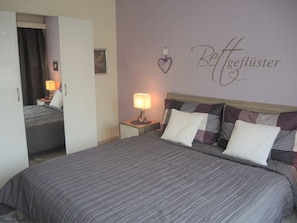 Een hotelkamer met een bed, nachtkastjes, een spiegel en een wand met een decoratie in de vorm van een hart en tekst.
