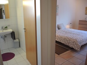 A hotel room with a bathroom, a bed with patterned bedding, a bedside table, and a lamp. - Apartment Tista by Interhome (Ascona)