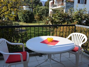 A balcony with a round table and two chairs, a yellow object on the table, and a view of a garden and buildings in the background. - Apartment Tista by Interhome (Ascona)