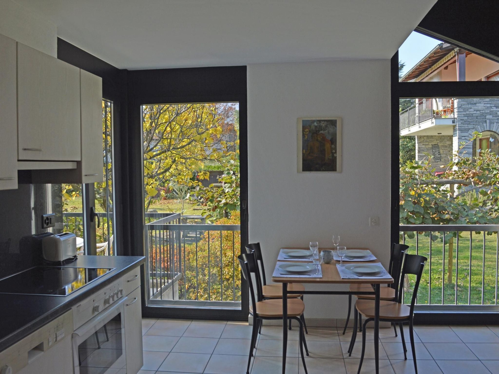 A modern kitchen with a dining area, large windows, and a view of a garden.