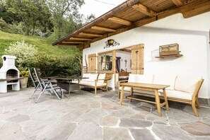 Un espace extérieur aménagé dans un style rustique, avec un sol en pierre, des meubles en bois et un bâtiment blanc doté de poutres en bois.