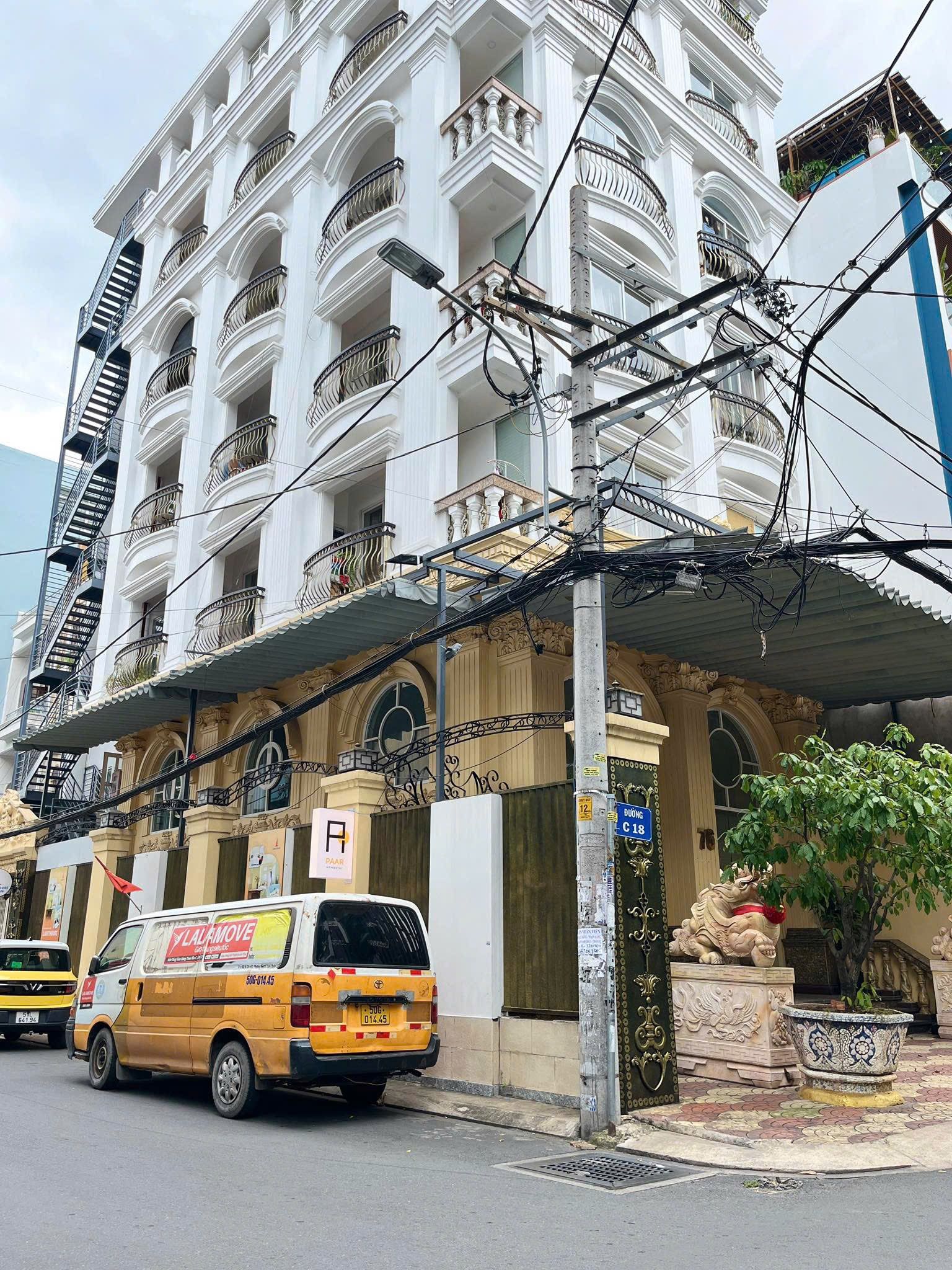 A multi-story building with balconies, a yellow van parked in front, and a sign indicating a parking area.