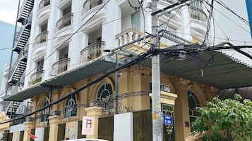 A multi-story building with balconies, a yellow van parked in front, and a sign indicating a parking area.