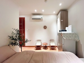 Ein Hotelzimmer mit einem Bett, zwei Stühlen, einem kleinen Tisch, einer Klimaanlage, einer Wanduhr und einer Tür.