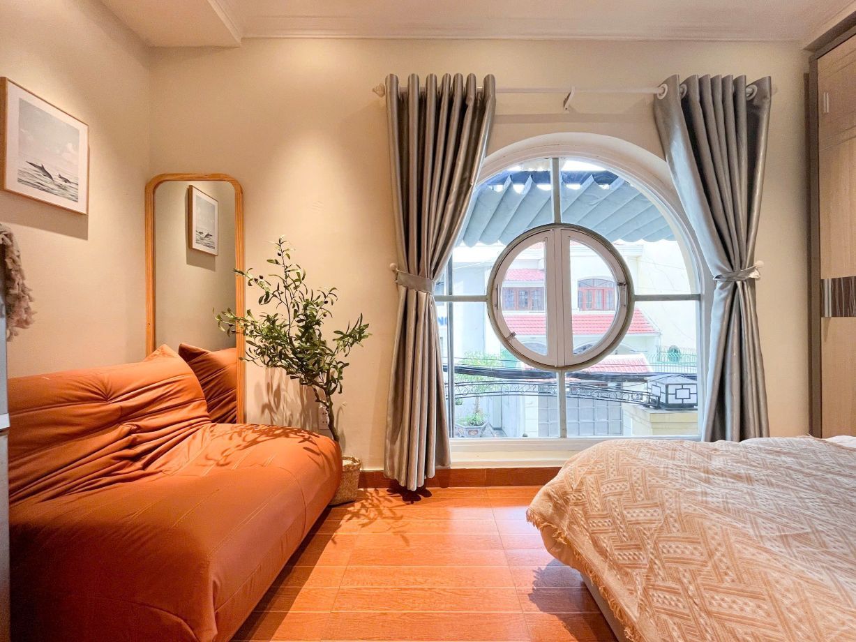 Een slaapkamer met een bed, een slaapbank, een raam met gordijnen, een plant en een spiegel.