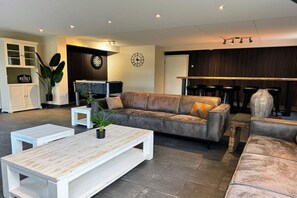 A modern living room with a leather sofa, white coffee table, and a bar area with stools. - Hopman de Rijklaan 6 (Vrouwenpolder)
